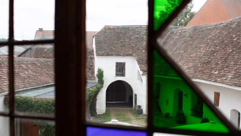 View through a stained glass window of an old courtyard with an arched gate and tiled roofs.