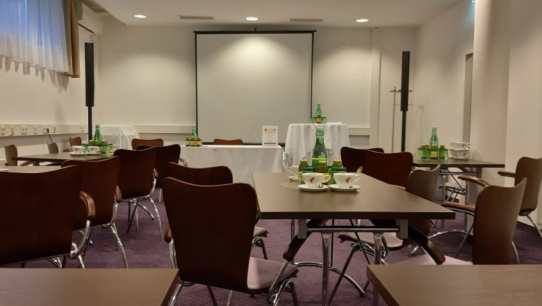 Seminar room with tables, chairs and drinks, projection screen in the background.