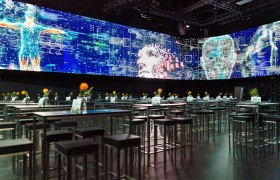 A modern showroom with digital projections and tables with flowers.