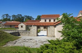 Reconstructed Roman buildings in Carnuntum with red tiled roofs and stone walls, surrounded by green vegetation.