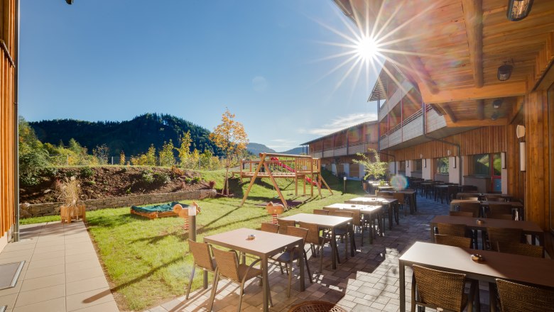 Terrace of the JUFA Hotel Annaberg with tables, chairs and playground in the background in the sunshine.