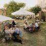 People sit at outdoor tables in a garden with parasols.