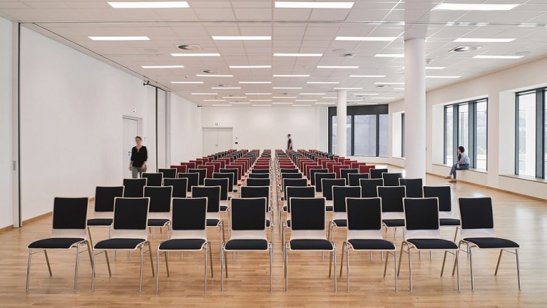 Empty conference room with rows of chairs and wooden floor.