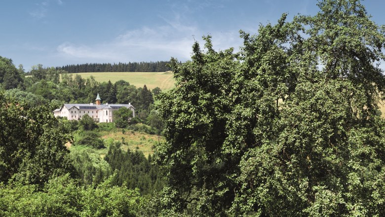 A hotel building in the middle of a green landscape with trees and hills in the background.