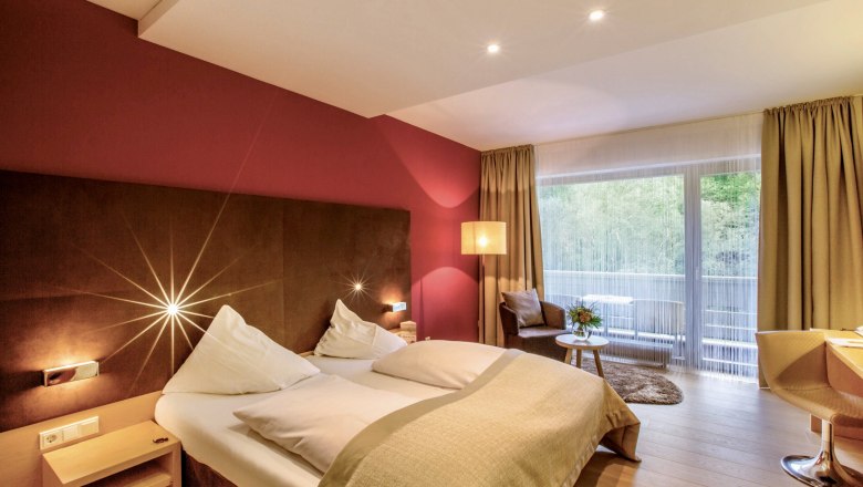 Modern hotel room with double bed, red wall, large window and seating area.
