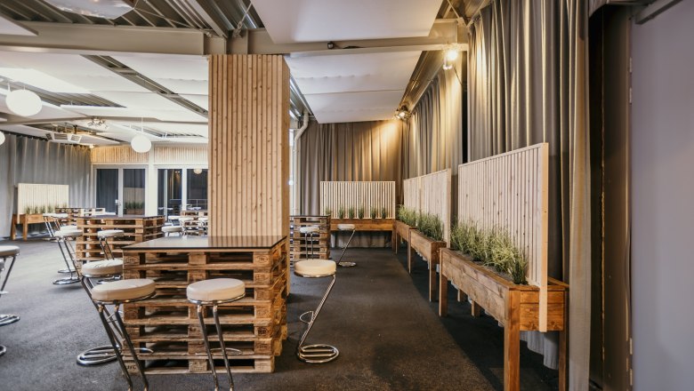 Interior view of the foyer of the ARENA NOVA congress hall with modern furniture made from pallets and plants.
