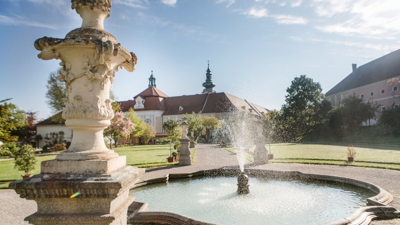 Fountain in the garden of Seitenstetten Abbey with baroque architecture in the background.