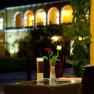 A table with a glass of beer and two roses in a vase, in the background an illuminated building with arches.