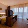 Modern hotel room with double bed, TV, desk and large windows with curtains.