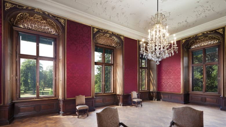 Elegant room in Eckartsau Castle with red walls, large windows and a chandelier.
