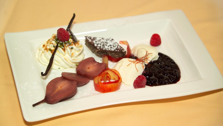 A dessert plate with various desserts, including cream, berries, chocolate cake and poached pears.
