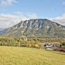 A panoramic view of a mountainous landscape with meadows in the foreground and a village in the background.