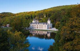 Hernstein Castle with reflection in the water, surrounded by trees and hills.
