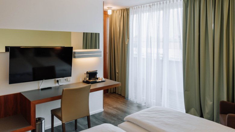 Modern hotel room with desk, TV and curtains.