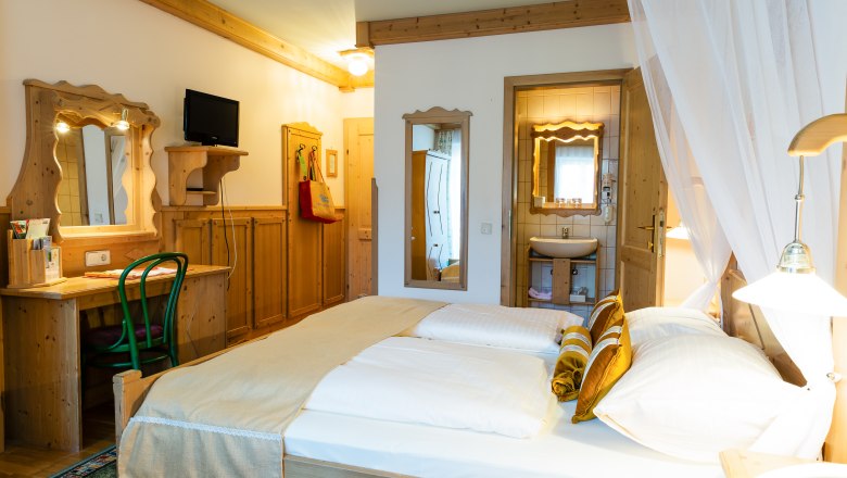 Comfortable hotel room with double bed, wooden furniture and small bathroom.