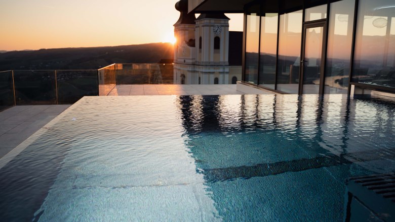 Infinity pool at sunset with a view of a building and the landscape.