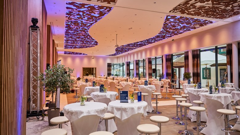 Interior view of a modern event hall with decorative ceiling and round tables.