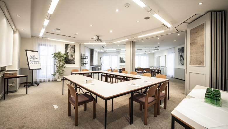 Conference room with U-shaped tables and chairs, flipchart and plants.