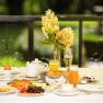 Breakfast table on the terrace with flowers, juice, bread rolls and eggs.
