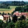 A large building with red roofs in a green, wooded landscape.