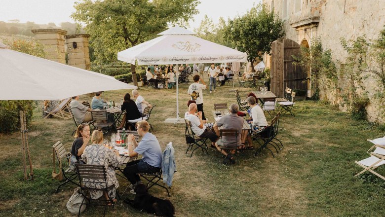 People sit at outdoor tables in a garden with parasols.