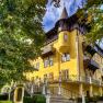 Historic yellow building with towers and decorations, surrounded by trees.