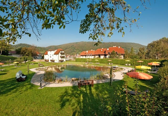 Garden area with pond, sun loungers and parasols, surrounded by buildings and hills.