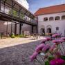 An inner courtyard with cobblestones, tables and chairs, surrounded by buildings with arcades and a modern balcony.