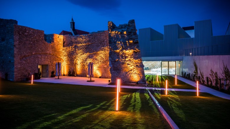 Illuminated ruins and modern architecture at night.