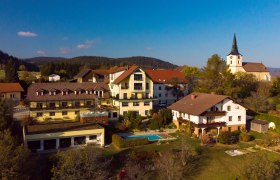 Aerial view of a village with a hotel, a pool and a church in the background.