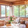 Elegant restaurant with laid tables, flowers and views of nature through large windows.