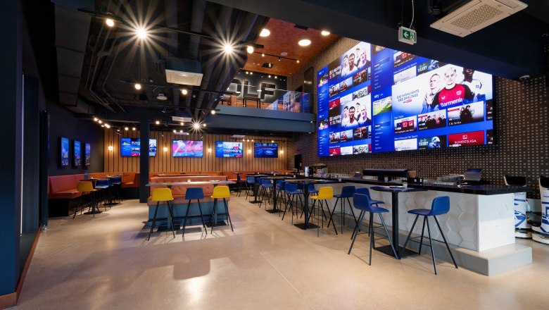 Interior view of a modern sports bar with large screens and colorful chairs.