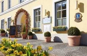 Entrance of a yellow building with flowers and signs.