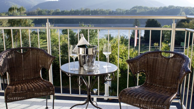 Two rattan chairs and a table with a champagne cooler on a terrace with a mountain view.