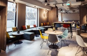 Modern hotel restaurant with colorful chairs and tables, large windows and stylish lighting.