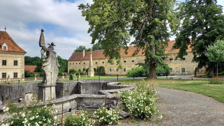 View of a historic castle complex with statue and garden.