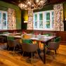 A hunting room with a wooden table, green chairs and antler chandelier.