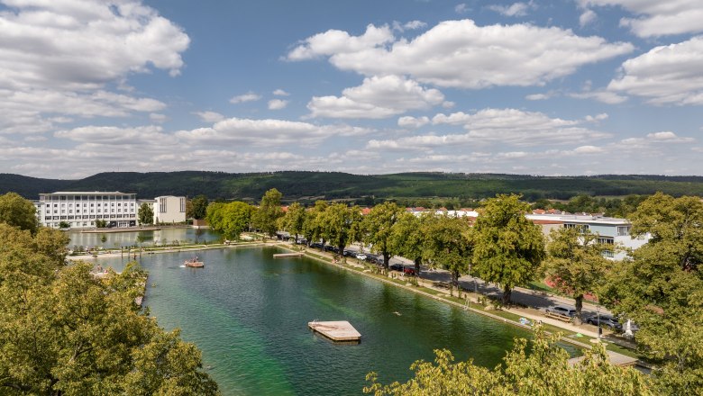 Aerial view of a lake with surrounding buildings and trees under a blue sky.