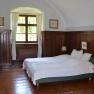 Bedroom with wooden walls, a double bed, a window with curtains and a chest of drawers with lamp.