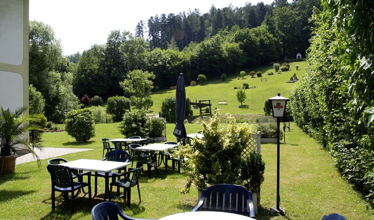 Garden with tables and chairs, surrounded by trees and meadows.