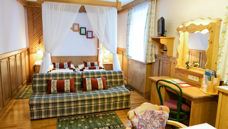Cozy hotel room with double bed, sofa, desk and mirror in rustic style.