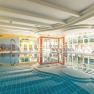 A bright indoor pool with sun loungers and a jet of water in the pool.