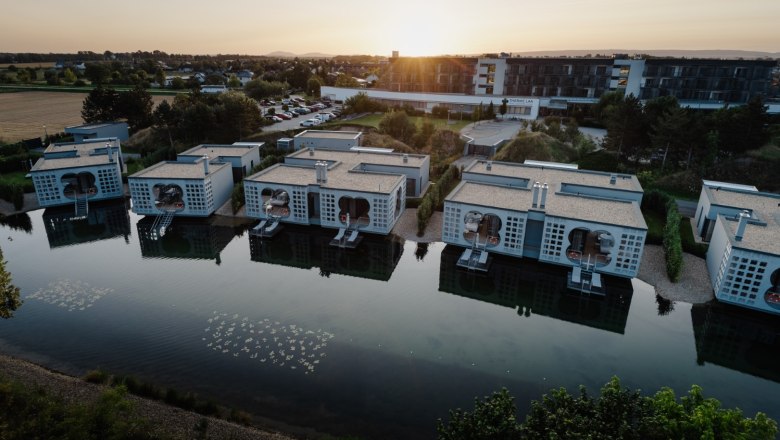 Aerial view of modern buildings on the waterfront at the Laa thermal spa resort at sunset.