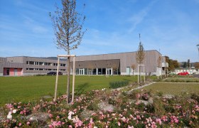 Modern building with wooden façade and well-kept gardens in the foreground.