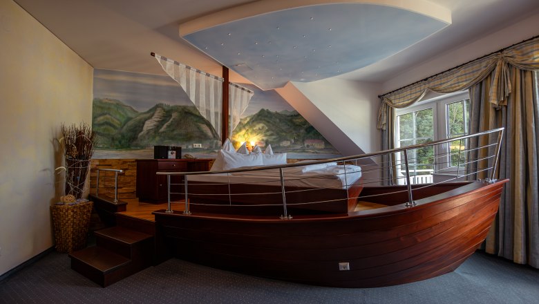 Hotel room with bed in the shape of a boat, wall painting of landscape, window with curtains.