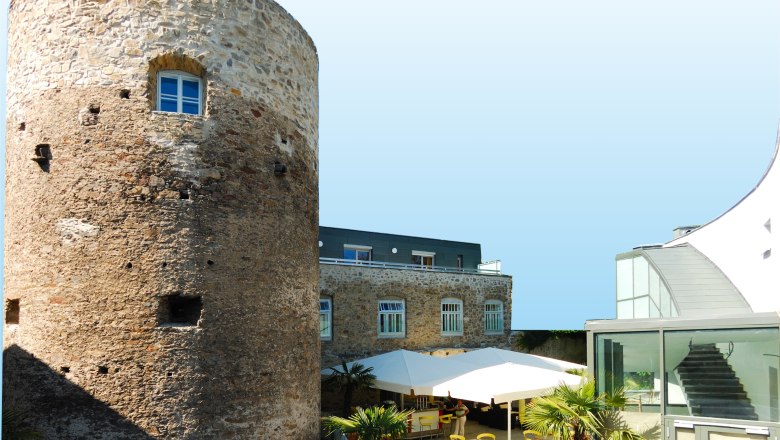 Historic tower next to modern building with terrace and parasols.