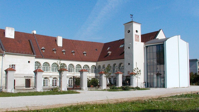 Katzelsdorf Castle with modern extension and historic building. White façade with rounded windows, red roof and large inner courtyard
