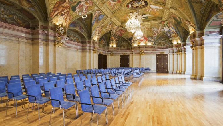 Interior view of the state parliament hall in the Palais Niederösterreich with blue chairs and artistically painted ceiling.