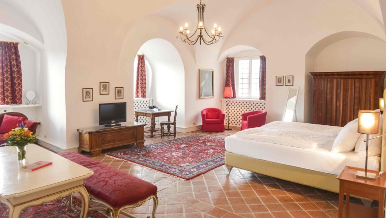 Luxurious suite with antique furniture, red carpets and curtains, a large bed and a chandelier.