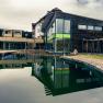 Modern wellness hotel with wooden fa&ccedil;ade and large pond in the foreground.